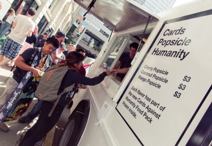 Group of people waiting in line at an ice cream truck with a sign for ice pops