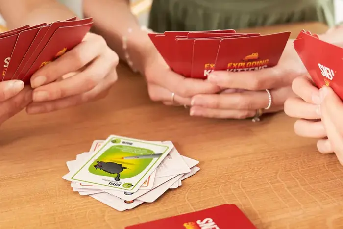 Closeup of three people's hands playing Exploding Kittens