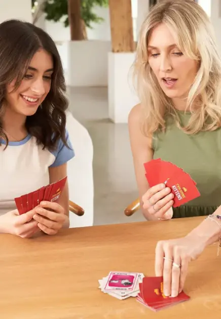 Two women sitting at a table playing Exploding Kittens