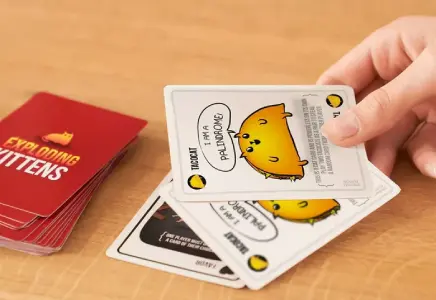 Closeup of Exploding Kittens deck of cards and a hand holding several cards face up